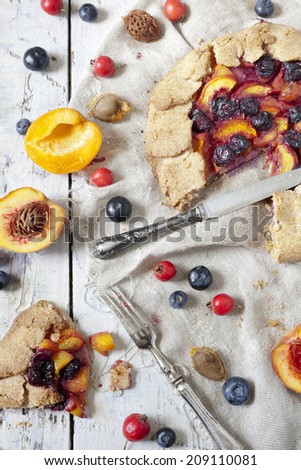 wholemeal french galette with fruits sliced apricots peaches and blueberries on vintage rustic background with fresh fruits and rosehip on wooden table