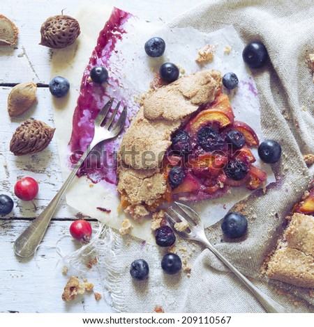 polaroid of wholemeal french galette with fruits sliced apricots peaches and blueberries on vintage rustic background with fresh fruits and rose hip on wooden table