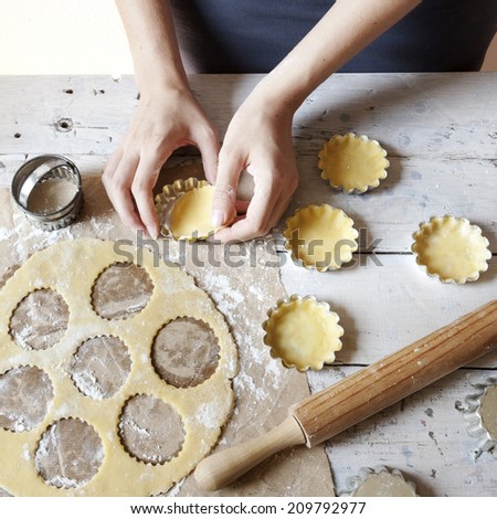girl hands making shortcrust pastry for little tart on molds on rustic background with rolling pin and flour on wooden white table