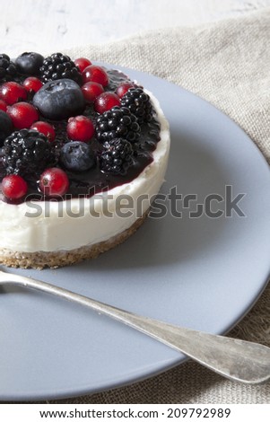 whole mini cheesecake with blackberries, blueberries and red currant on plate with fork