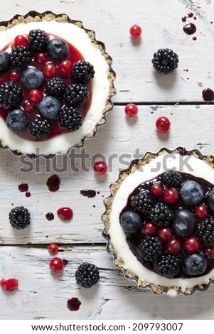 two mini cheesecake with blackberries, blueberries and red currant on molds on rustic background with berries on wooden white table