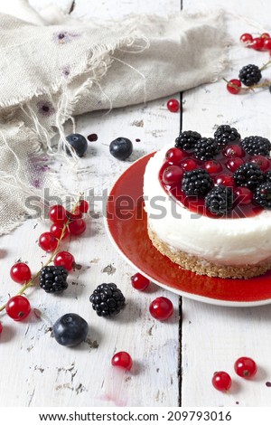 whole mini cheesecake with blackberries, blueberries and red currant on plate and berries on wooden white table