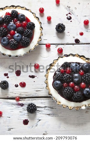 two mini cheesecake with blackberries, blueberries and red currant on molds on rustic background with berries on wooden white table