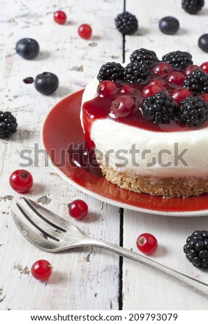 whole mini cheesecake with blackberries, blueberries and red currant on plate with fork and berries on wooden white table