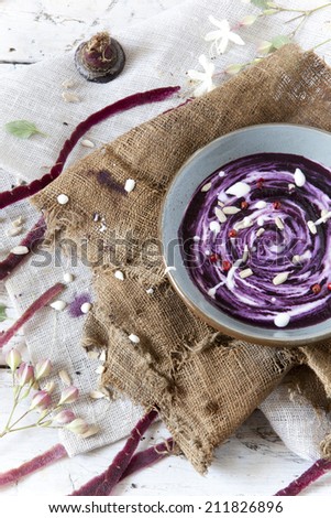 purple carrot cream soup with sour milk cream and pink peppercorn on bowl on rustic vintage background with carrot peels and burlap