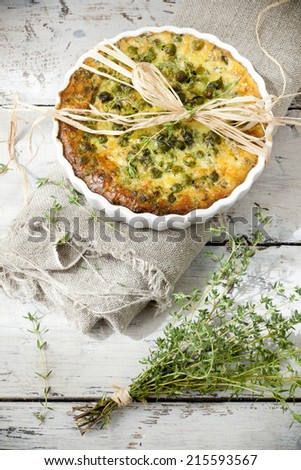 rustic vegetables french quiche with peas on baking dish on vintage background on wooden table with thyme bouquet