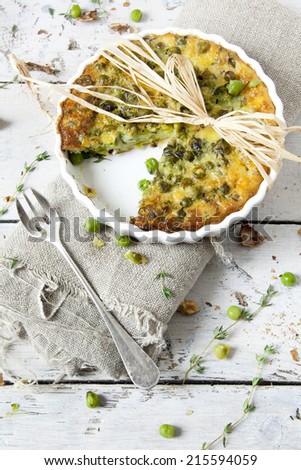 rustic vegetables french quiche with peas on baking dish on vintage background on wooden table with fork and burlap