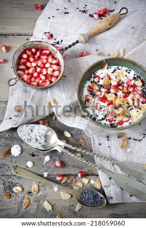 pomegranate grains on vintage strainer and little portion of yogurt with seed and almond slices with spoon on wooden table