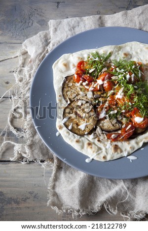 homemade mediterranean flatbread with grilled eggplants, roasted tomatoes, wild fennel herb and yogurt on plate on wooden table