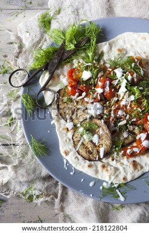 homemade mediterranean flatbread with grilled eggplants, roasted tomatoes, wild fennel herb and yogurt on plate with vintage scissor