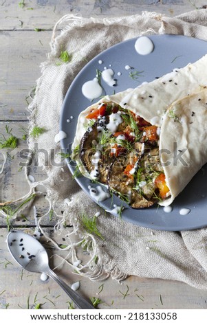 vegetarian flatbread roll with grilled eggplants, roasted tomatoes, wild fennel herb and seed with yogurt on plate on wooden table