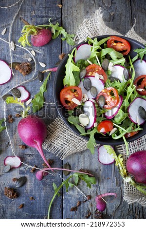 rocket salad on bowl with radish and tomatoes slices and sunflowers seed on rustic blue wooden table