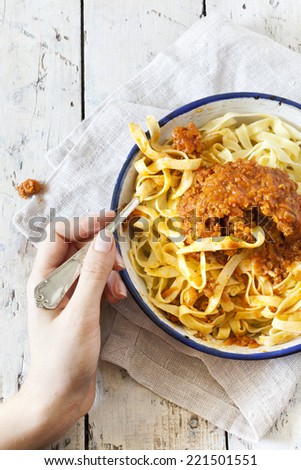 hand with forkful of handmade pasta with ragout sauce on vintage plate