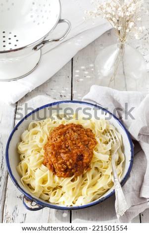 handmade pasta with ragout sauce on plate on vintage white table with colander and flowers