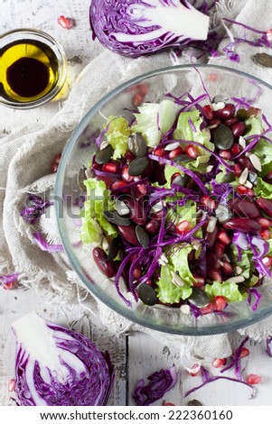 mixed salad on bowl with red beans, seeds and purple cabbage with separate seasoning on white table