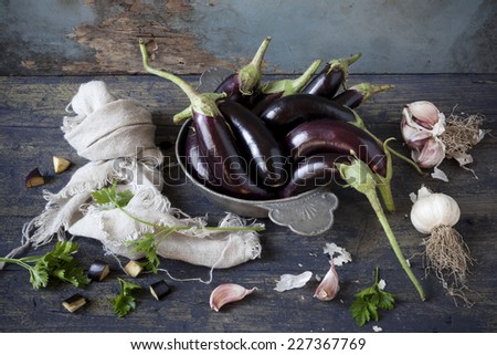 group of long eggplants on vintage plate on wooden table with garlic and parsley and frayed cloth