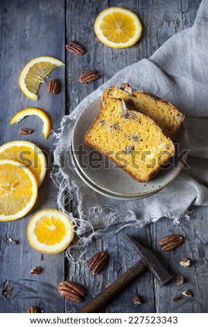 two slices of citrus cake on plate on table with pecan walnuts and orange slices and little hammer