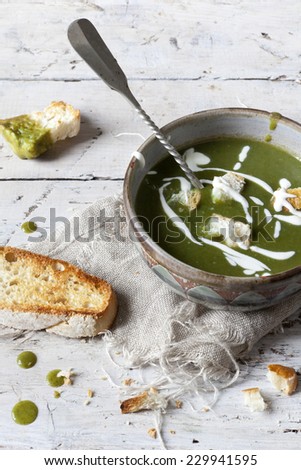 homemade peas and spinach cream soup with sour cream on bowl on rustic table with toasted bread croutons