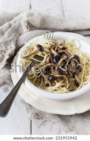forkful of italian pasta spaghetti with fresh pioppini mushrooms on plate on white table with napkin