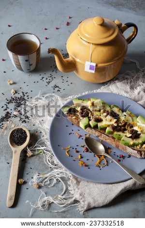 wholemeal vegan toast with avocado slices and black sesame seeds on table with teapot and frayed napkin