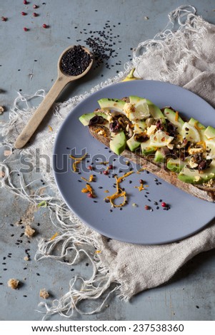 wholemeal vegan toast with avocado slices, lemon, orange peel, pink pepper and black sesame seeds on plate with frayed napkin