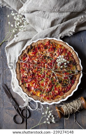 baked red peppers tart on quiche mold on rustic table with cloth, scissor and spool