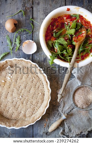 making a wholemeal quiche with red peppers and rocket on ceramic mold on rustic wooden table with napkin