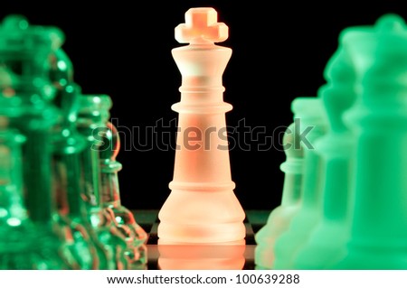 red king and rows of green glass chess pieces is standing on board in dark