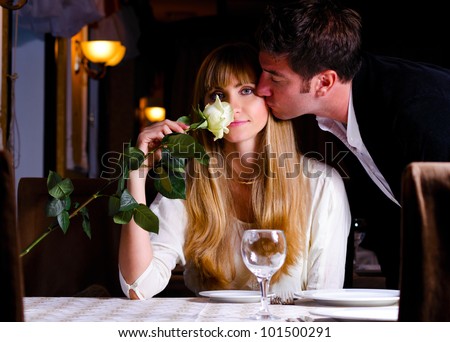 man is kissing woman sitting at restaurant