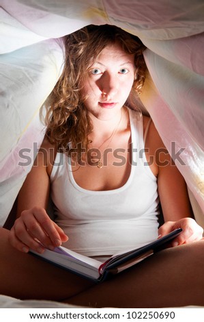 woman is reading under cover in bed and writing her diary