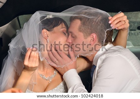 just married couple is kissing in car under bridal veil