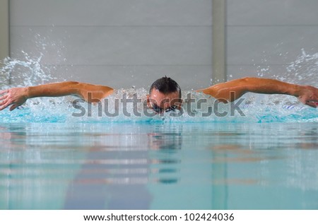 man swims using the butterfly stroke in indoor pool