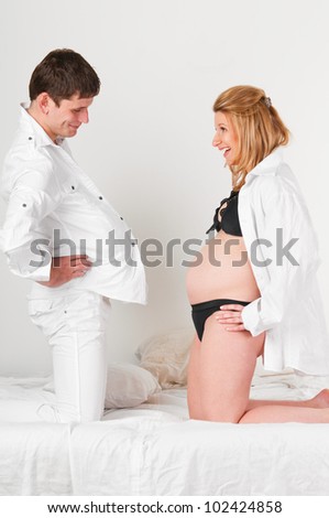 man with pillow under shirt and his pregnant wife are comparing their bellies.