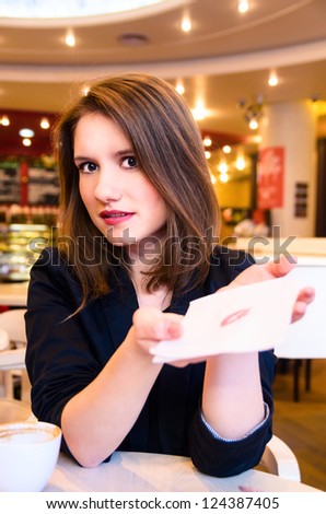 young woman is flirting and showing lip print on serviette in modern cafe