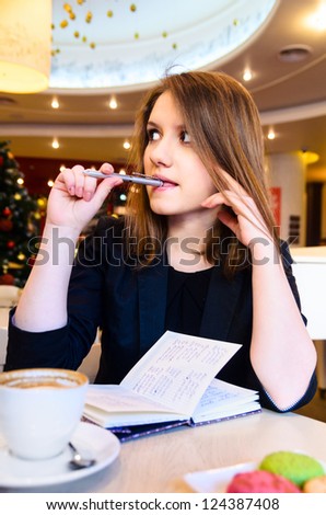 young woman with notebook is thinking in modern cafe