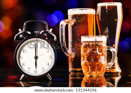 time to drink beer. glasses of fresh lager beer with clock on black with reflection