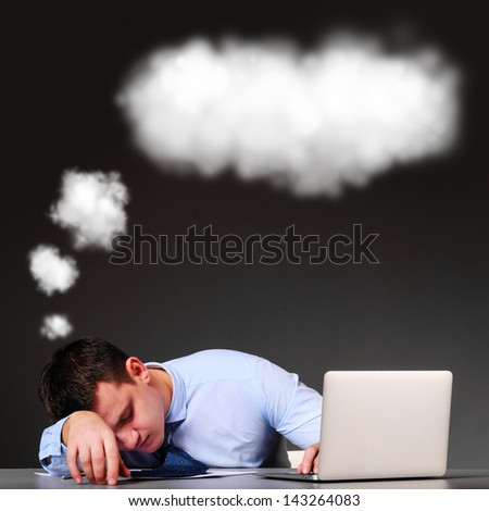 tired businessman is sleeping at his table with laptop and a cloud above his head