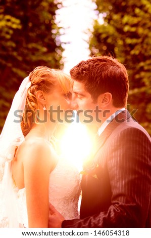 bride and groom is kissing with joined hands to the sunset