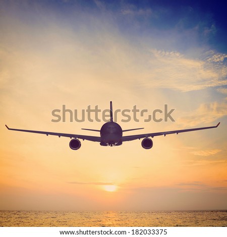 airplane is flying over the sea at sunset