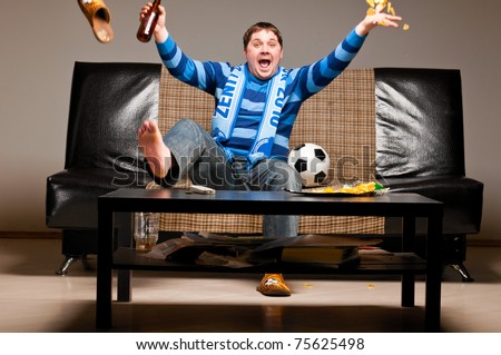 soccer fan is sitting on sofa with beer at home