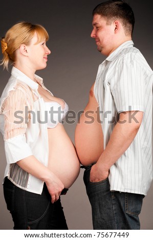 man and pregnant woman is standing face to face and showing their bellies, side view