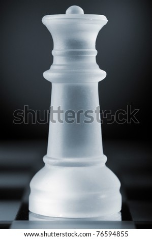 glass chess queen is standing on board in dark