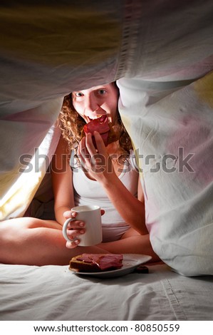 woman is sitting under cover in bed and eating