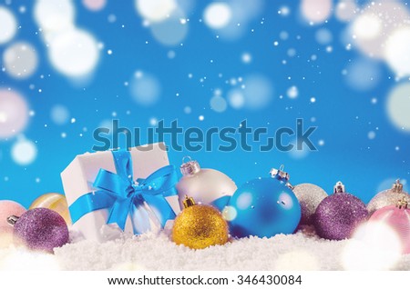 white decorative christmas gift box with ribbon and balls on snow against blue festive background