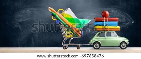 Back to school sale background. Car delivering shopping cart with accessories, books and apple against blackboard.