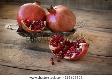Three red juicy pomegranate on plate lying on wooden table from old boards