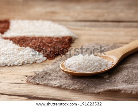 white rice in a wooden spoon on the sackcloth on an old wooden table