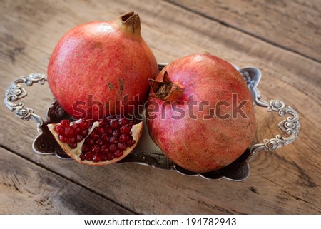 red juicy pomegranate on silver plate lying on wooden table from old boards