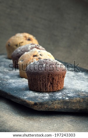 Four chocolate and vanilla muffin on rustic bakery peel with sugar powder