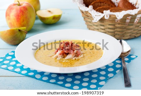 Indian soup (Potage Mulligatawny) with apple curry, bacon and basil in white soup bowl on blue desk with polka dot napkin